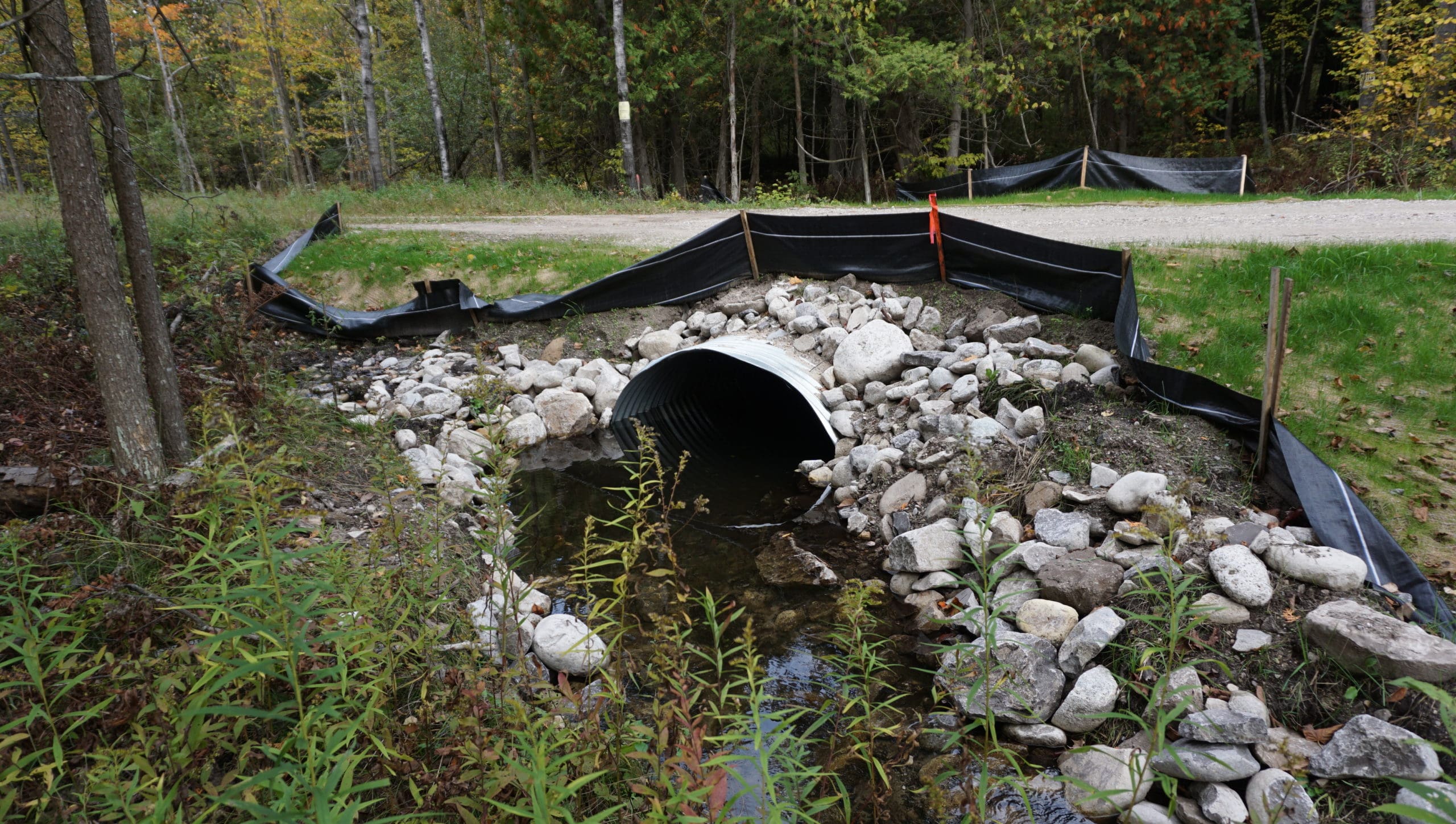 picture of a tributary after restoration, with a metal culvert surrounded by rock rip rap, with a road crossing above 