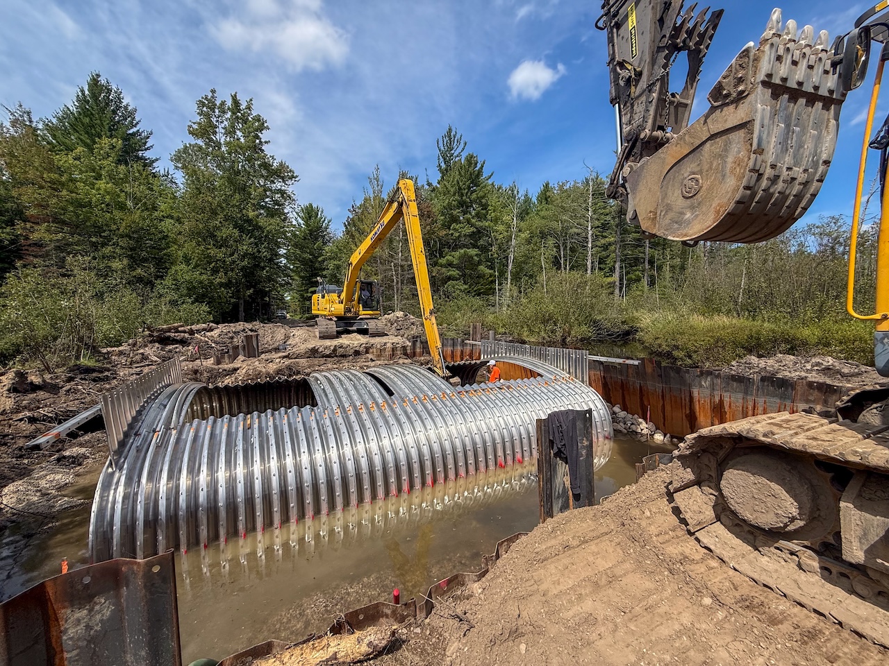 IMG_1753 Large corrugated metal stream crossing being installed at a tributary to the North Branch Manistee River and Grass Lake Road, with excavators and construction equipment working around the partially submerged structure.